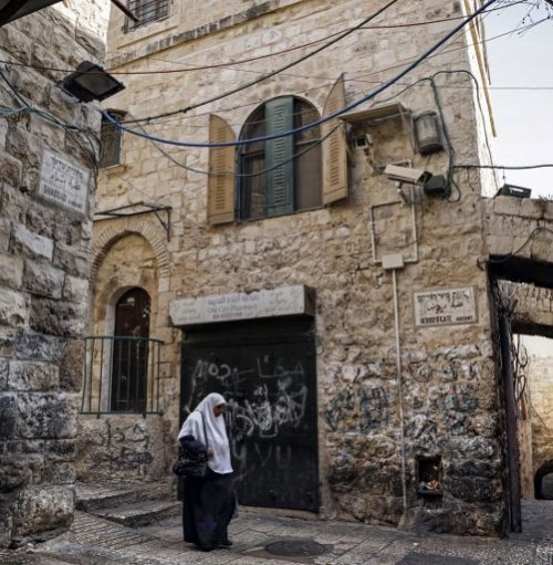 A Palestinian woman walks past a house in the Muslim Quarter of the Old City of Jerusalem which was bought by Israeli settlers, on December 4, 2019. - In an alley in Jerusalem's Old City, a three-storey building has become a symbol of Palestinian fears they are losing precious ground in the historic area. The Mamluk-style building in the Old City's Muslim quarter was controversially sold to Israeli settlers -- an action that many Palestinians consider treason. (Photo by THOMAS COEX / AFP)